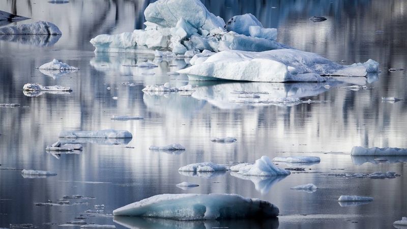 Scattered lumps of ice in a still, reflective lake.