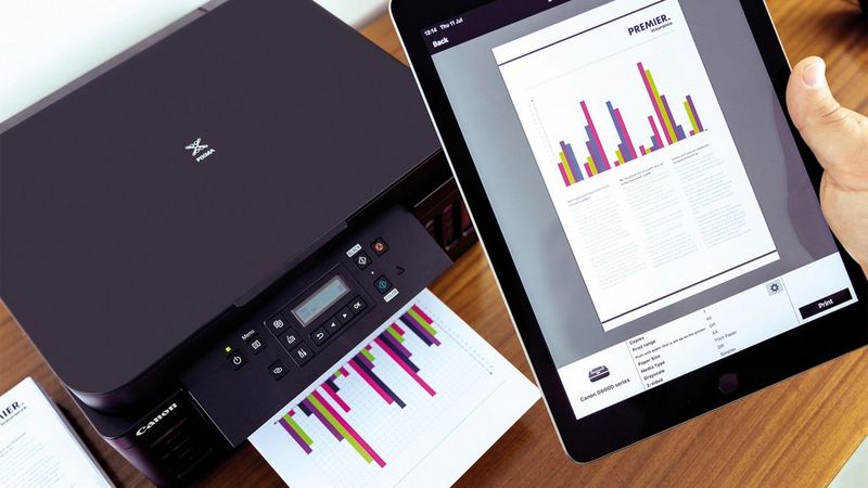 A man using the Canon PRINT app on a tablet to print a document of a bar graph on a Canon PIXMA G6050.
