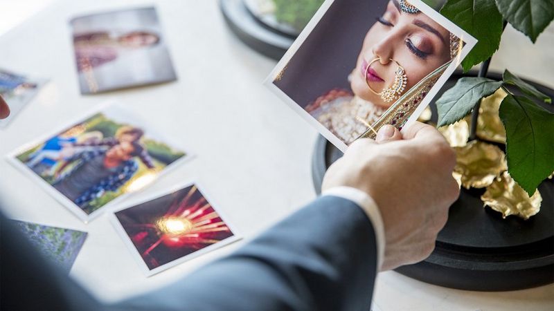 A man holding a picture of a woman, with more sentimental photos laid out on a table. 