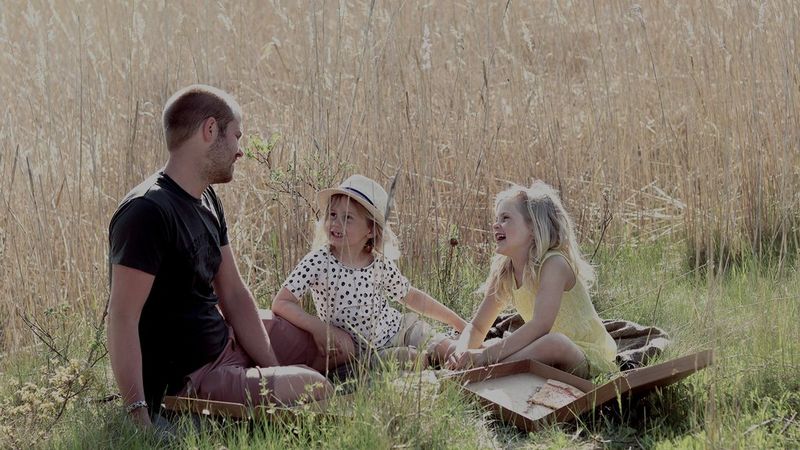 A man and two children sit in a sunny field enjoying a picnic. Photo by Hannah Clark on a Canon EOS 250D.