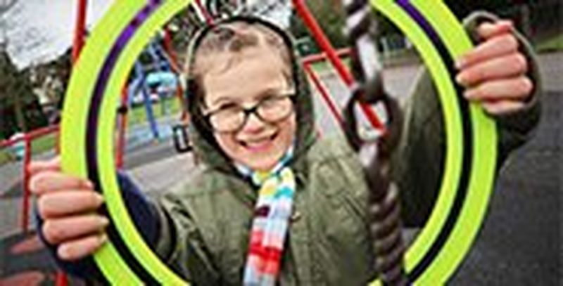 A girl in a playwark holds a frisbee up, framing her face.