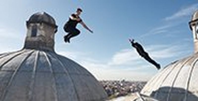 Two young men dressed in black leap around on a rooftop between Turkish domes with stone lanterns on top.