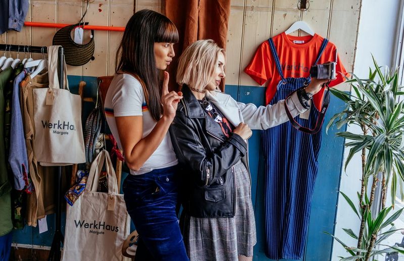 Two women pose in front of a camera in a clothes shop.