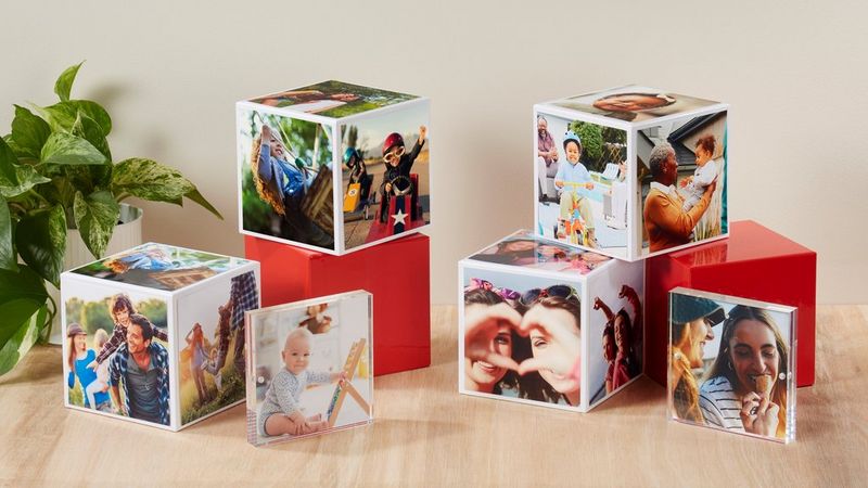 Several Canon Photo Cubes, some stacked on top of each other, on a wooden table with a green plant in the corner.
