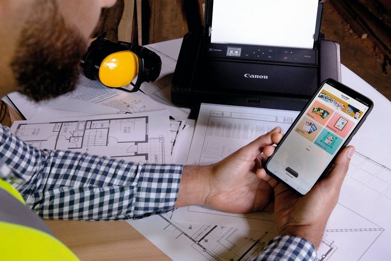 A man in a high-vis jacket prints out documents from his smartphone on a Canon PIXMA TR150 printer.