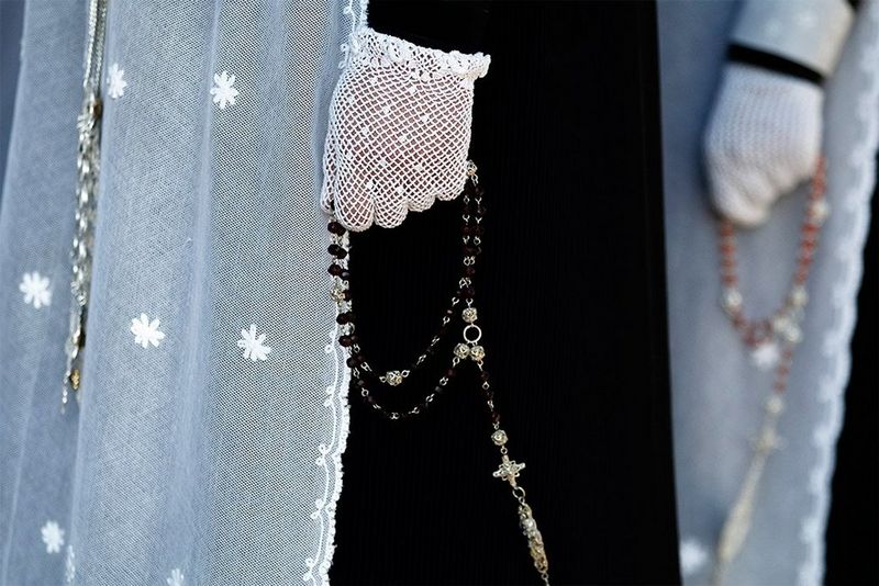 Close-up of women wearing religious dress and lace gloves, holding rosary beads.