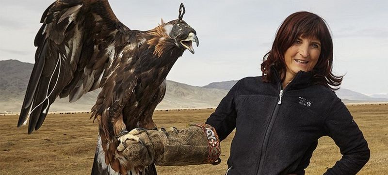 Photographer Alessandra Meniconzi wears a falconry glove and holds an eagle, amid a mountainous landscape.