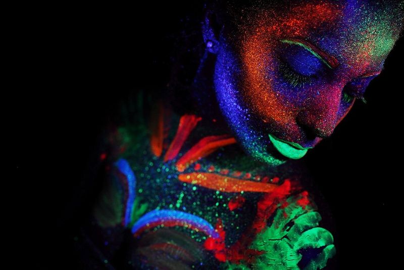Colourful patterns of body paint glow on the skin of a woman photographed under UV light with a Canon EOS R.