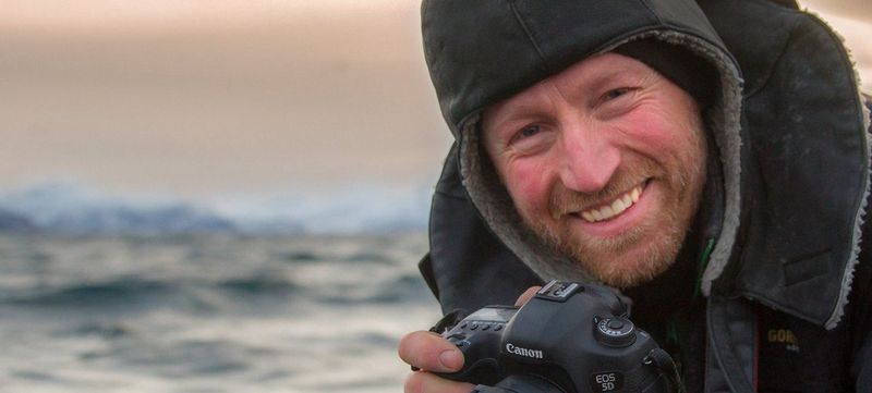 Audun Rikardsen, wearing a warm coat with a hood, holds a Canon camera.