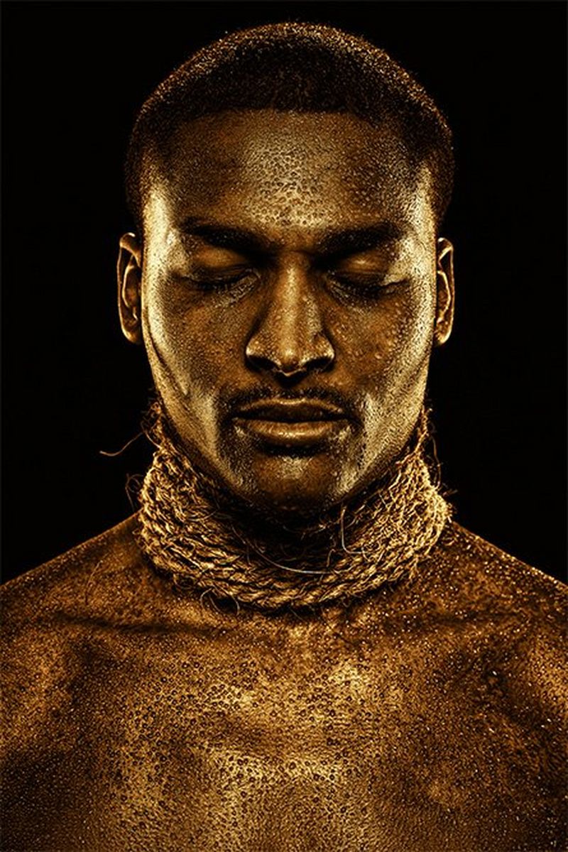 A man with gold-painted skin wears strings of rope around his neck.