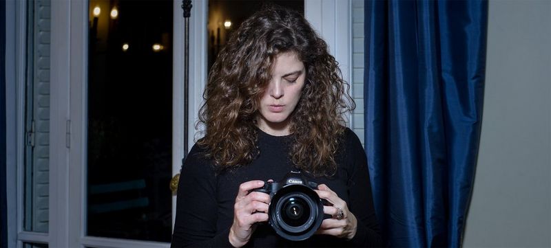 Photographer Carolina Arantes looks down at a Canon camera in her hands.