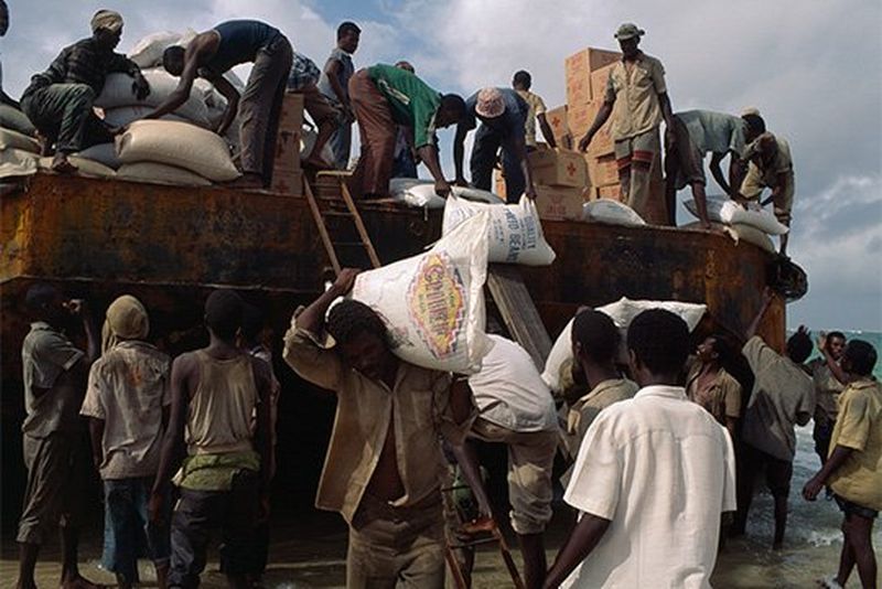 Men unload large sacks from the top of a bus.