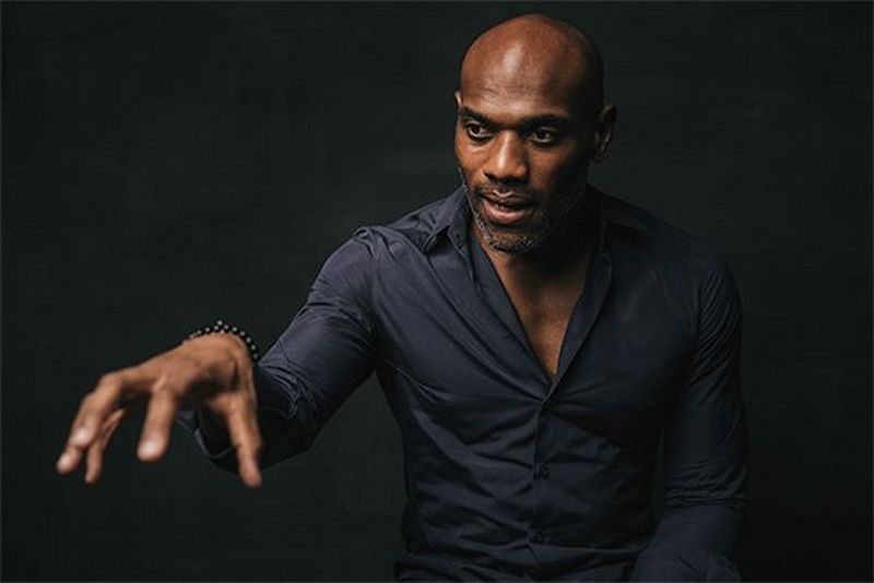 A man in a dark blue shirt gesturing with one hand.