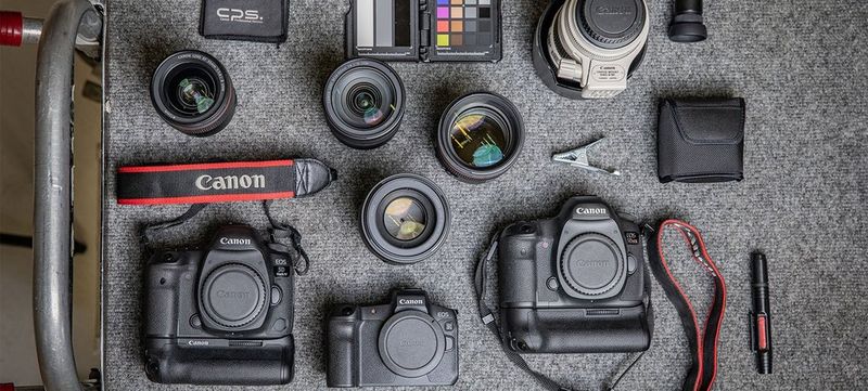 A Canon EOS R camera in the middle of a table, surrounded by two other cameras, various lenses and other equipment.