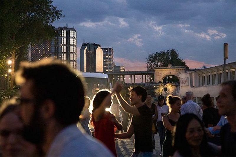 Outside, towers are seen in the background as people dance in front of them.