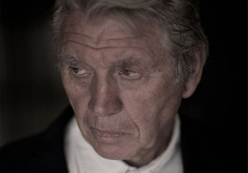 Sir Don McCullin, dressed in a white shirt and black jacket, poses for a portrait shot. 