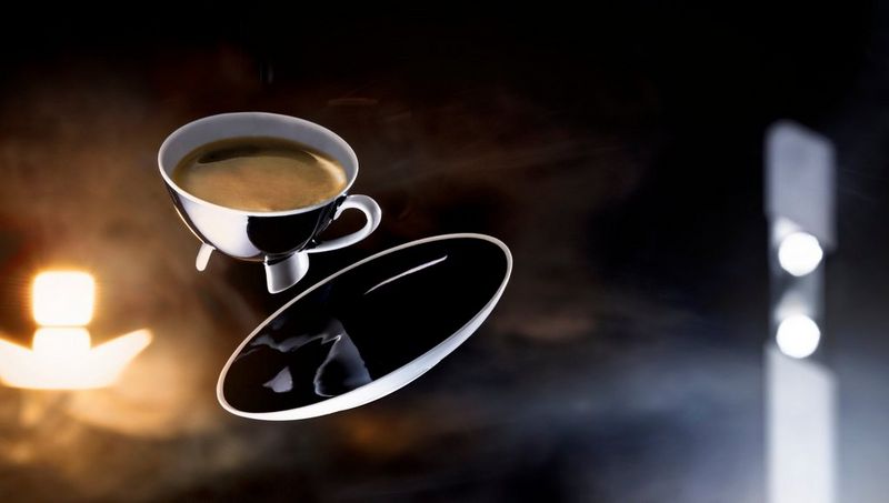 A metal cup of coffee and saucer appear to float in the air. Photo by Eberhard Schuy