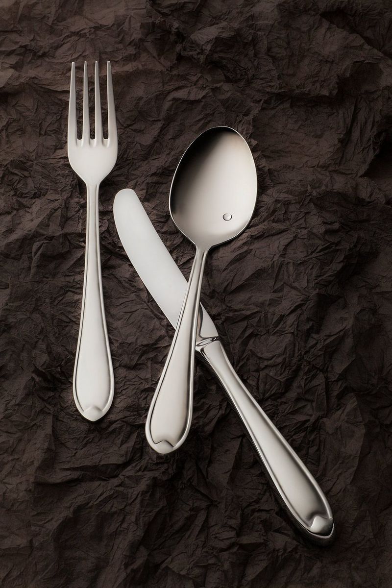 A close-up of a fork, knife and spoon on a dark background. Photo by Eberhard Schuy