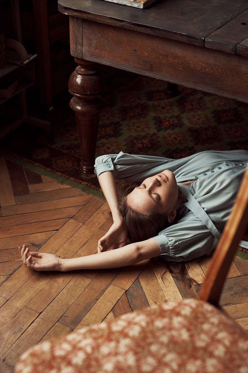 A woman lies underneath a table with her arms above her head. Taken by Jaroslav Monchak.