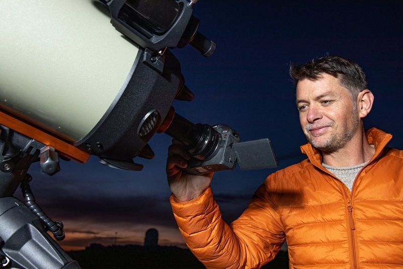 Fergus Kennedy holds a Canon EOS Ra to a large telescope, the tilt screen angled upwards.