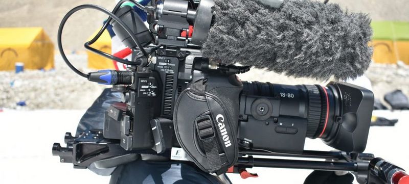 Filmmaker Sam Tongue holds a Canon EOS C200 cinema camera on his shoulder fitted with a Canon CN-E18-80mm T4.4 L IS KAS S lens.
