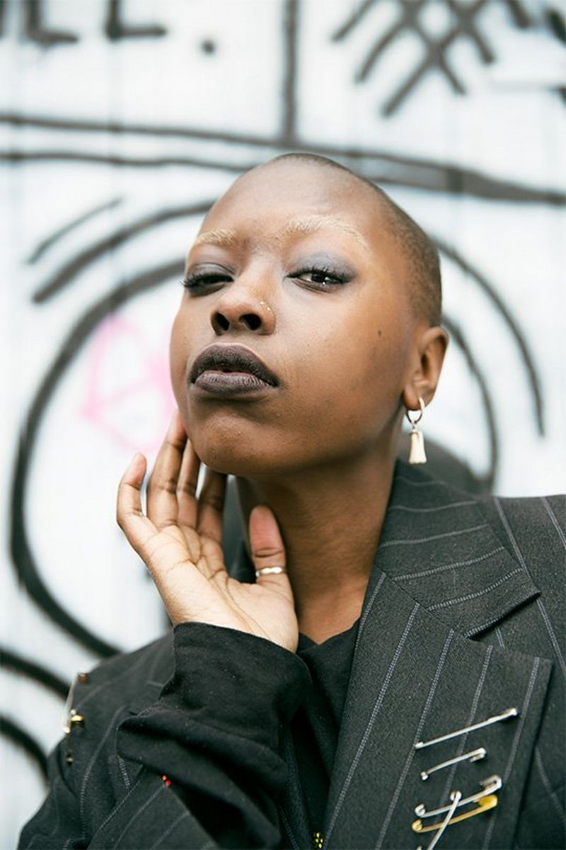 A female model with shaved head poses in front of graffiti. Photo by Rianna Gayle on a Canon EOS-1D X Mark II.