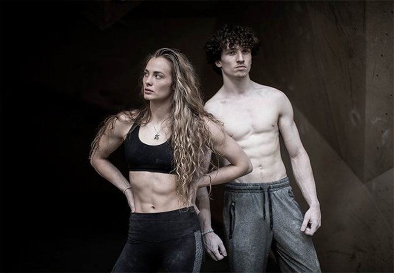 A female climber stands with hands on hips, with a male climber behind her.