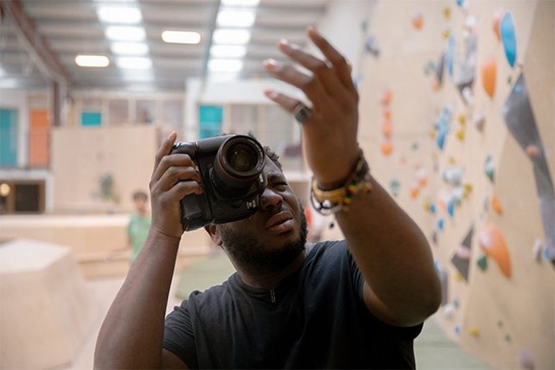 Francis Augusto gestures to a climber as he holds his Canon EOS 5D Mark IV to one eye.