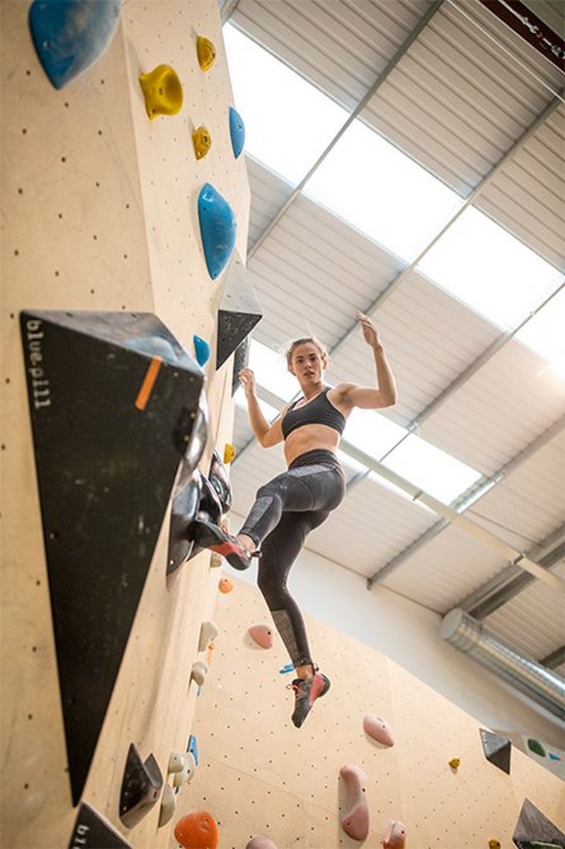 A female athlete moving between handholds, one foot on a hold and her other limbs seeming to float in the air.