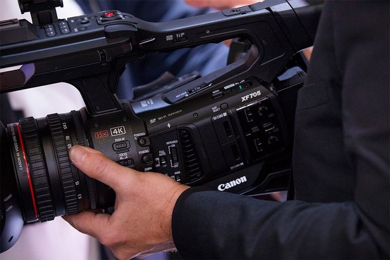 A man’s hands hold a Canon XF705 video camera.
