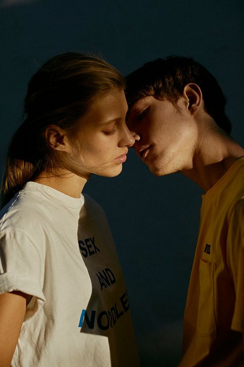 Two young models are poised to kiss, a shadow cast in between them.