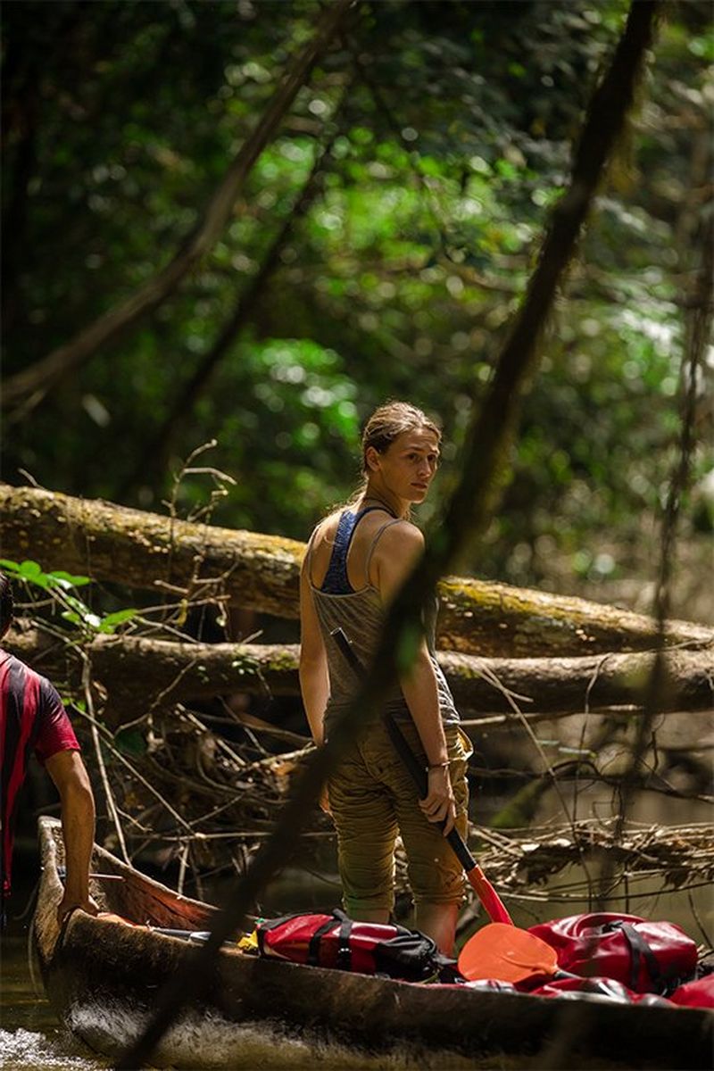 Laura Bingham stands in a canoe on a river bank.