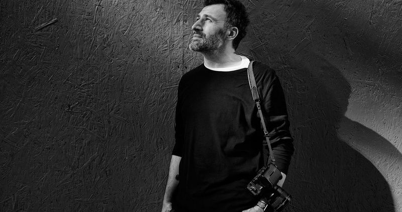 Photographer Maciek Nabrdalik wears a Canon DSLR camera over his shoulder and looks up to the sky.