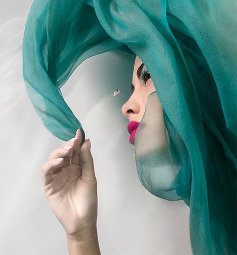 A close-up of a woman in profile with blue scarf and pink lipstick; a single air bubble rises past her face.