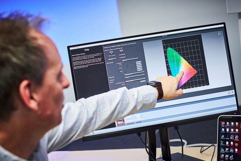 Een man wijst naar een computerscherm waarop een kleurenprofielkaart wordt weergegeven.