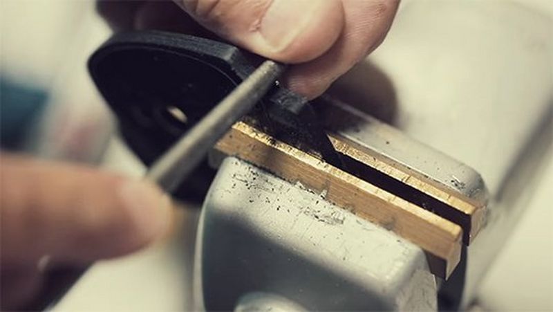 A close-up of a man&#39;s hands filing part of a spectacle frame held in a vice.
