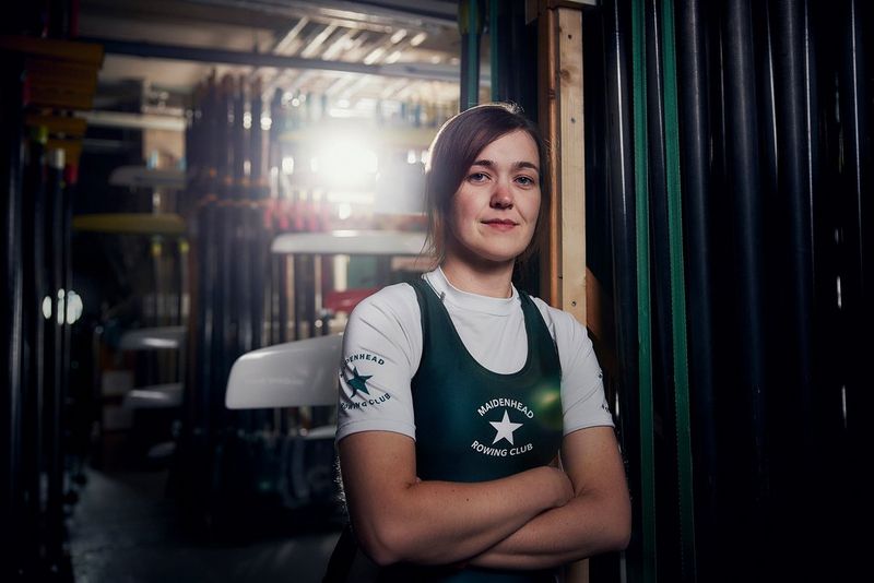 A woman stands in the equipment shed wearing her rowing kit. 