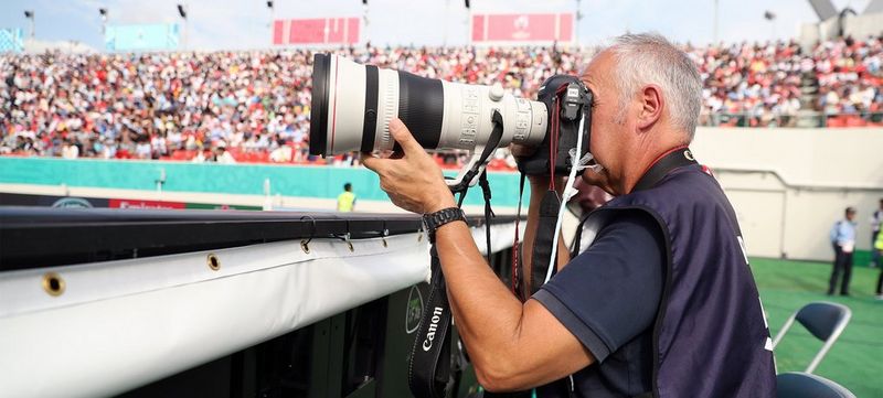 Dave Rogers at the side of the pitch looks through a Canon camera.