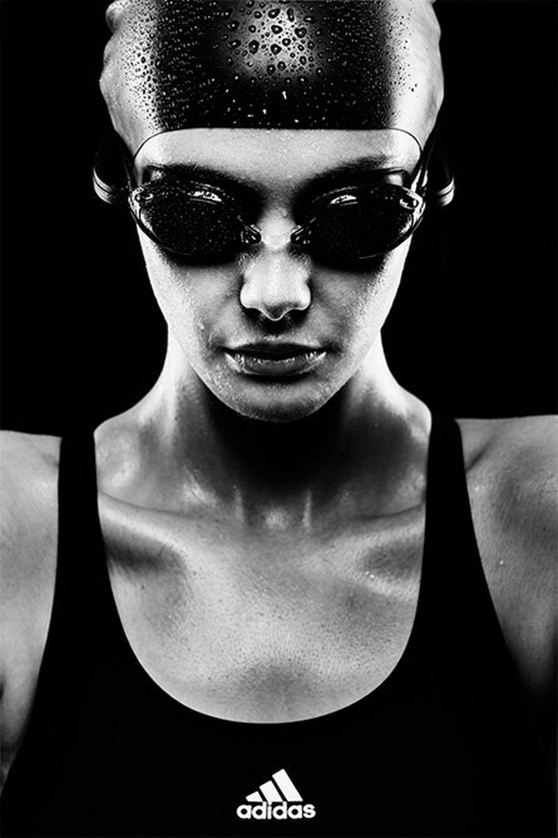 A high-contrast mono image of the head and shoulders of a female swimmer wearing goggles and a cap
