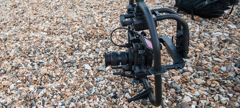 A Canon EOS C200 camera fitted in a gimbal sat on pebbles.