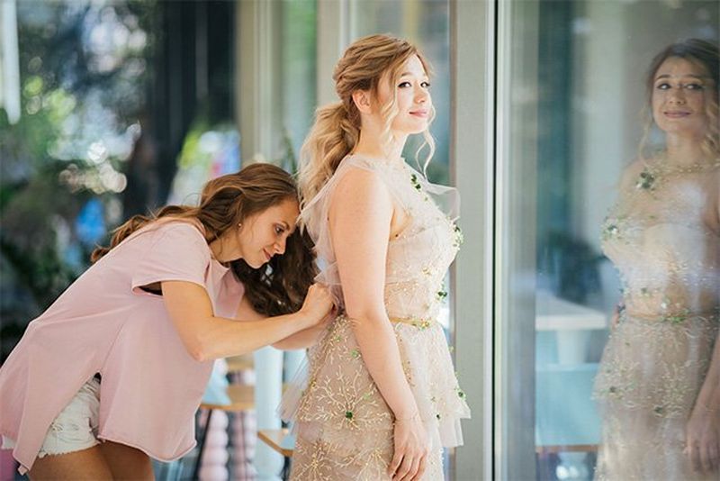 A woman bends to adjust the back of a bride's dress.