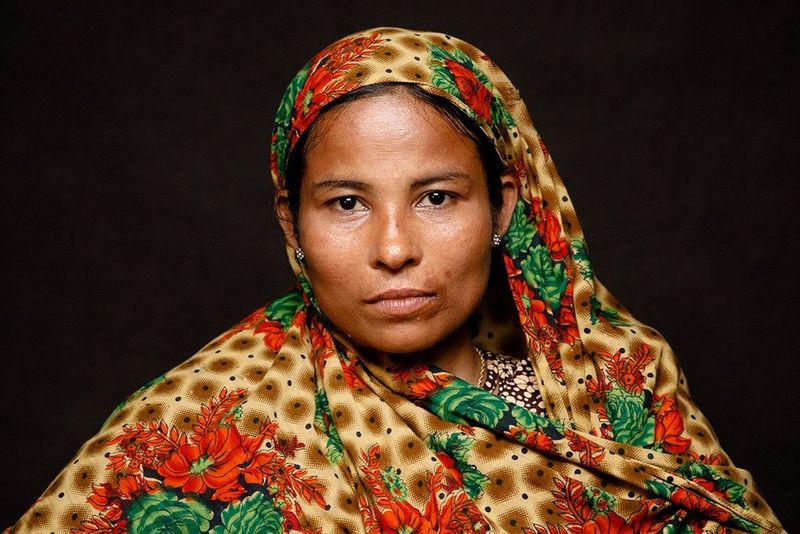 A woman wears a silken headscarf with brown, green and red floral patterns.