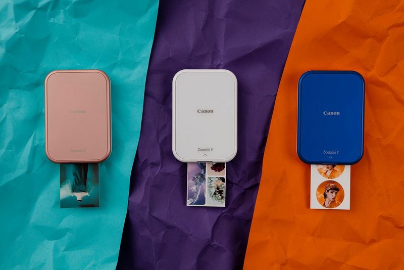 ثلاث طابعات Zoemini 2 من Canon باللون الوردي الذهبي والأبيض اللؤلئي والأزرق الداكن موضوعة على قطع ملونة من الورق المجعد، وكل منها تطبع صورة مختلفة.