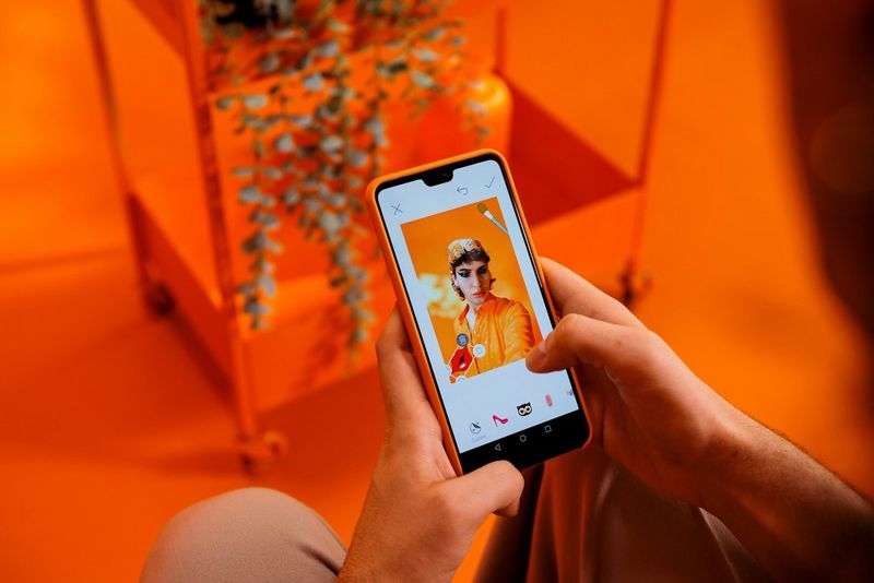 Aplicaţia Canon Mini Print afişată pe un telefon mobil, prezentând un bărbat care pozează în faţa camerei cu autocolante digitale prezente.