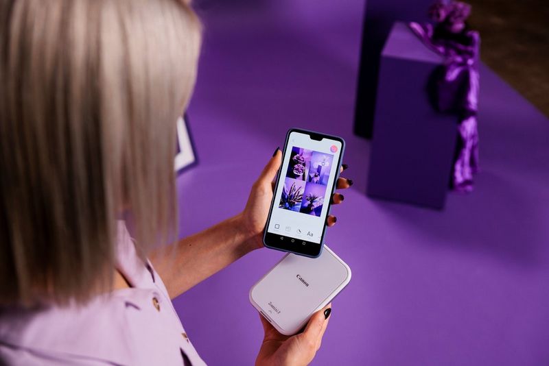 Een paar handen houdt een smartphone en een Canon Zoemini 2-printer vast en gebruikt de Canon Mini Print-app om een collage te maken.