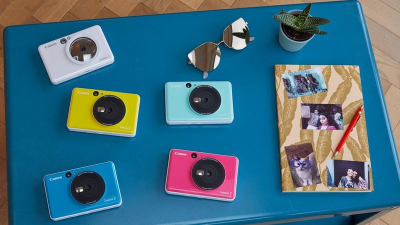 Canon Zoemini C and Canon Zoemini S on a table with a notebook with pictures stuck to it.