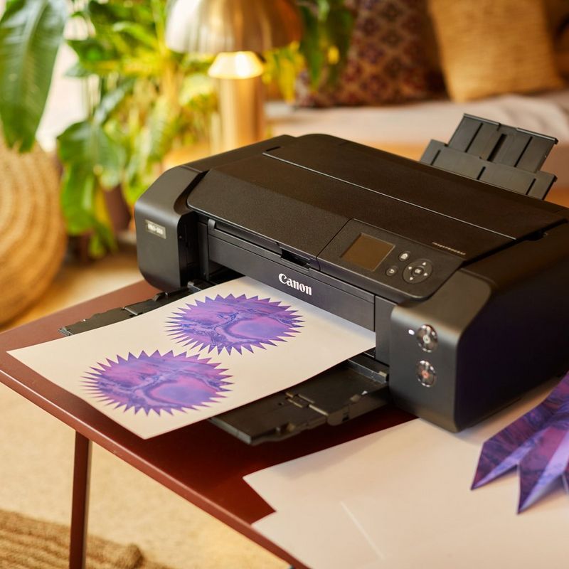 A piece of paper with two purple designs sits on the paper tray of a Canon imagePROGRAF PRO-300 printer
