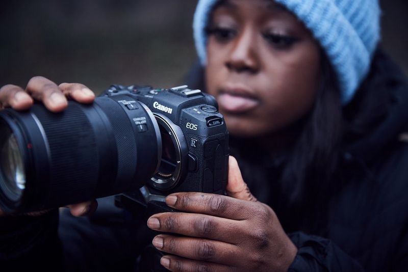 A young woman in a blue winter hat holding a Canon EOS RP camera.