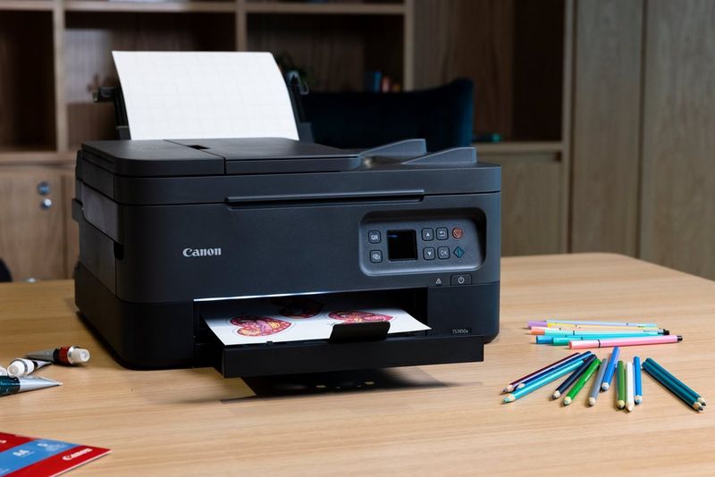 Een Canon PIXMA-printer staat op een houten bureau en er ligt een aantal kleurpotloden naast. Er worden kleurrijke vellen papier geprint.