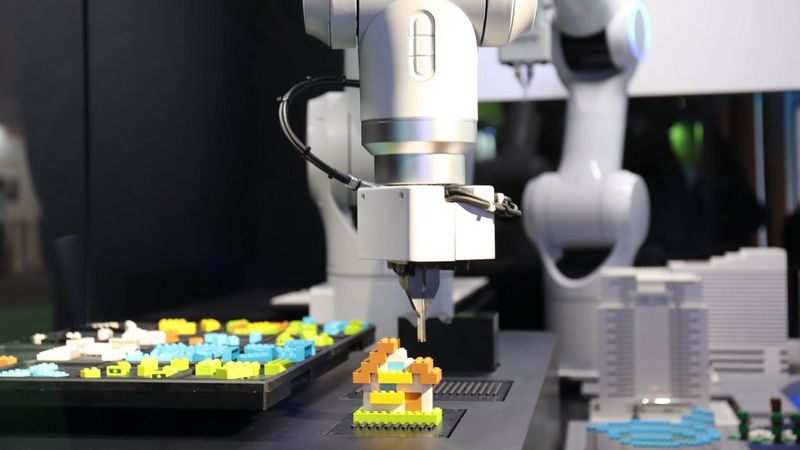 A robot arm builds a tiny house from Lego.